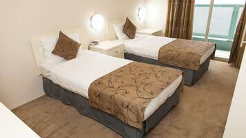 A hotel room with two beds, each with a pillow and a bedside table. There are wall sconces above the beds and a window with curtains.