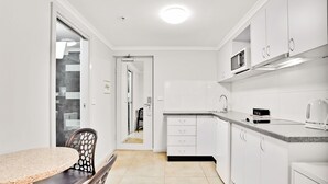A modern kitchen with white cabinets, a granite countertop, and a microwave. There is a dining area with a round table and chairs. - Carlton Lygon Lodge (Carlton)