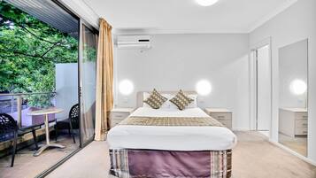 Un dormitorio moderno con una cama grande, mesitas de noche, una puerta de vidrio que da a un espacio exterior y vistas a zonas verdes.