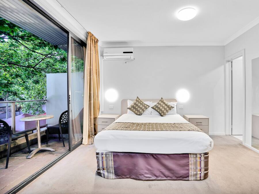 Un dormitorio moderno con una cama grande, mesitas de noche, una puerta de vidrio que da a un espacio exterior y vistas a zonas verdes.