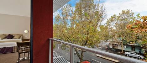 A hotel room with a balcony overlooking a street and trees.