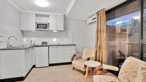A modern kitchen with white cabinets, a microwave, and a coffee maker. There are two chairs with a floral pattern and a small table. - Carlton Lygon Lodge (Carlton)