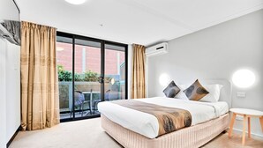 A modern bedroom with a large bed, a small table, and a view of a brick building through a sliding glass door. - Carlton Lygon Lodge (Carlton)
