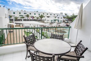A balcony with a round table and chairs, overlooking a courtyard with buildings and palm trees. - Club Del Carmen (Tías)