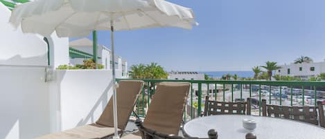 A balcony with two beige lounge chairs, a round table, and a white umbrella.