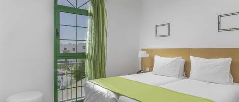 Camera d'albergo con un letto, un comodino, una lampada, una tenda verde e vista sull'esterno.