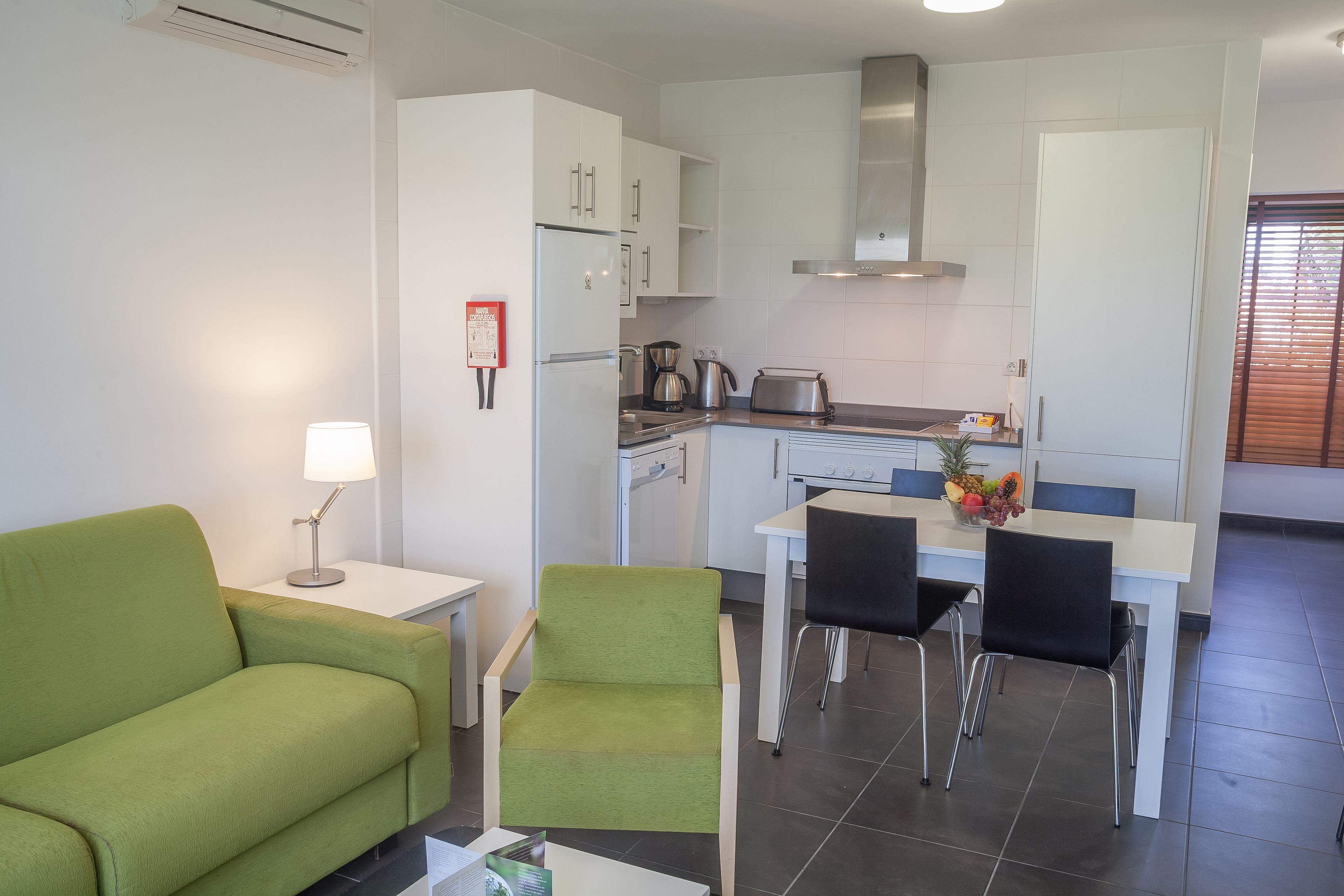 Cocina moderna con armarios blancos, campana extractora de acero inoxidable y comedor con mesa y sillas.
