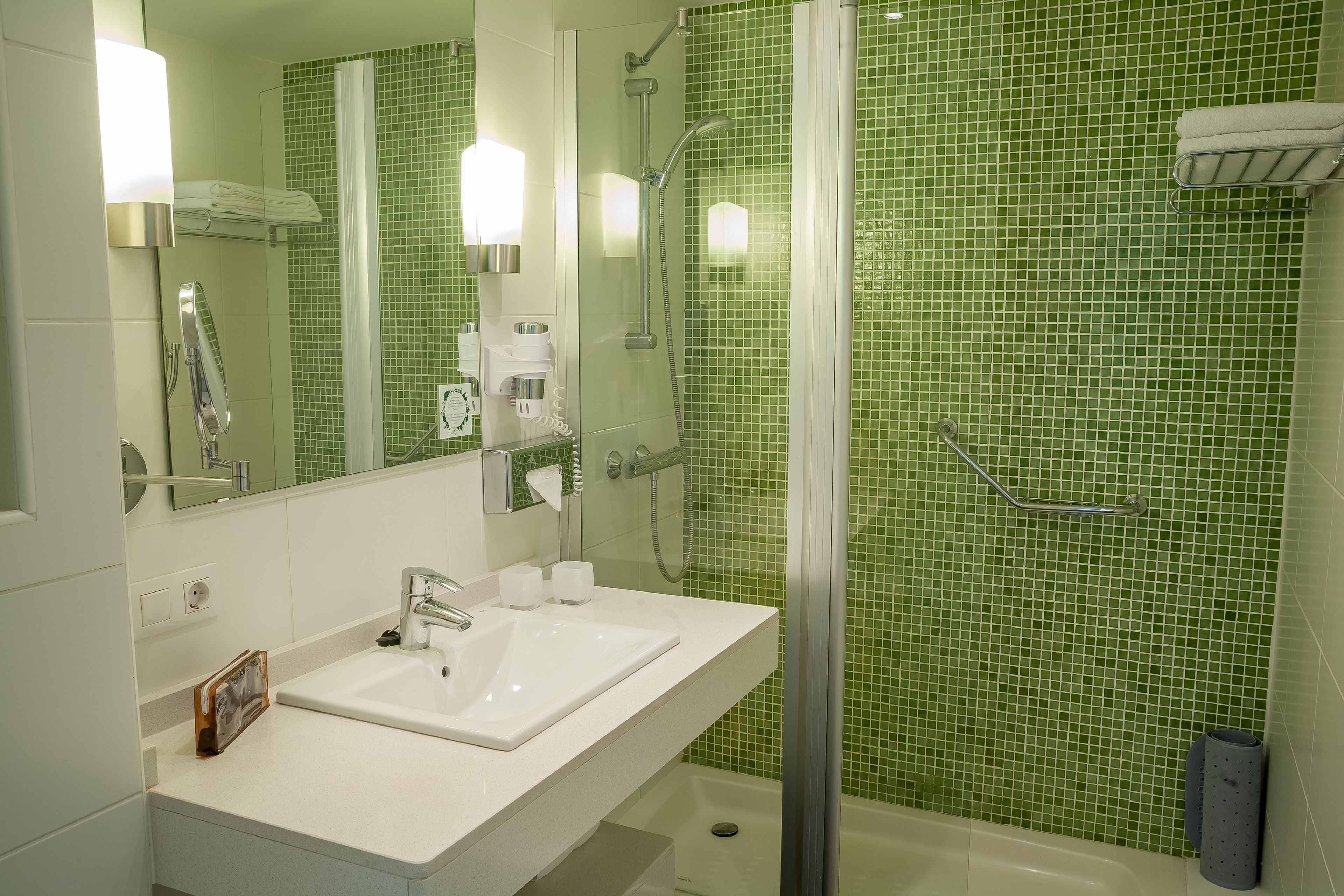 A bathroom with a white sink, a glass shower enclosure, and green tiled walls.