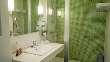 Um banheiro com pia branca, box de chuveiro em vidro e paredes revestidas de azulejos verdes.