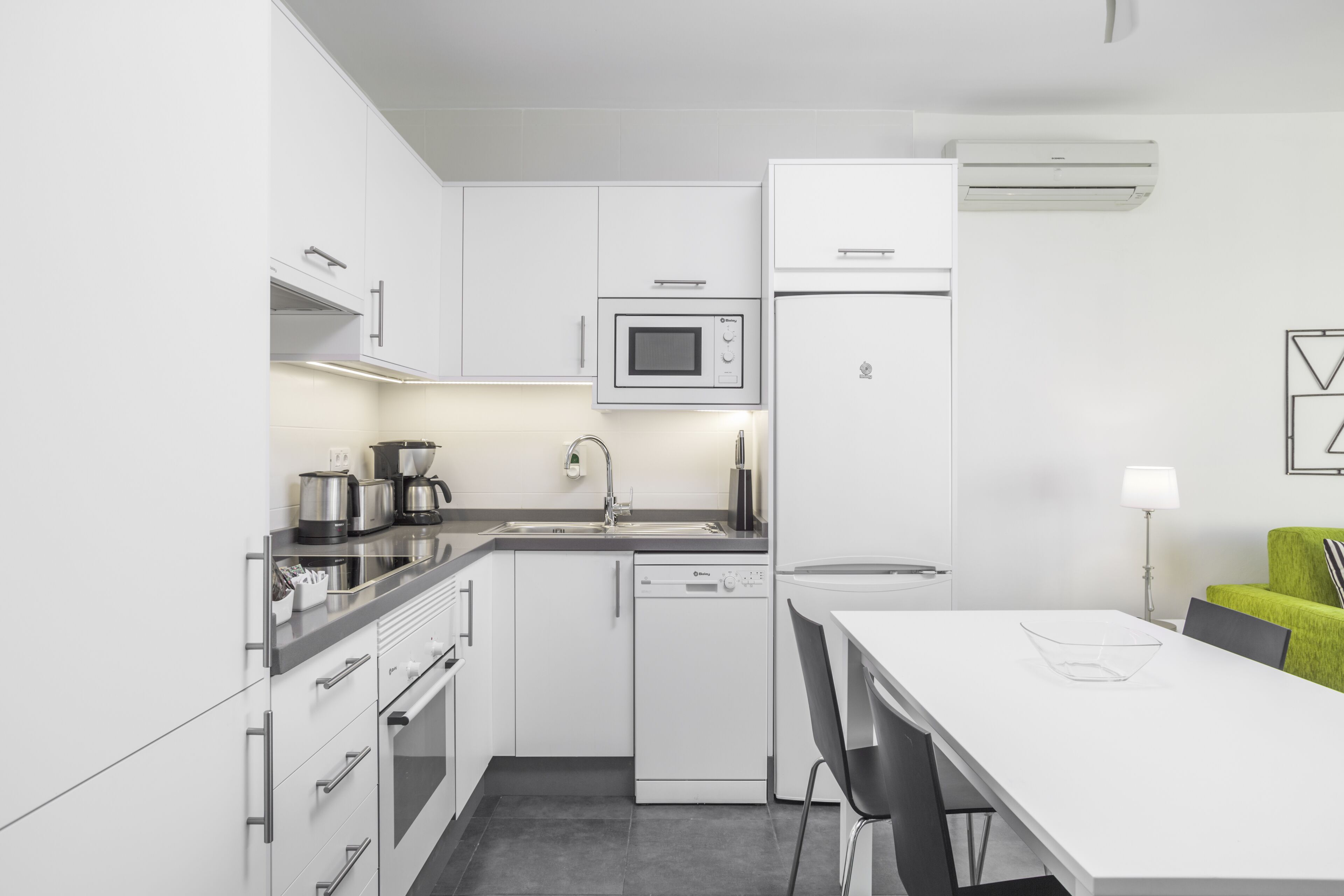 Una cocina moderna con armarios blancos, microondas, refrigerador y lavavajillas.