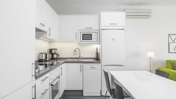 Una cocina moderna con armarios blancos, microondas, refrigerador y lavavajillas.