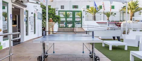 An outdoor area with a ping pong table, white benches, and a building entrance.