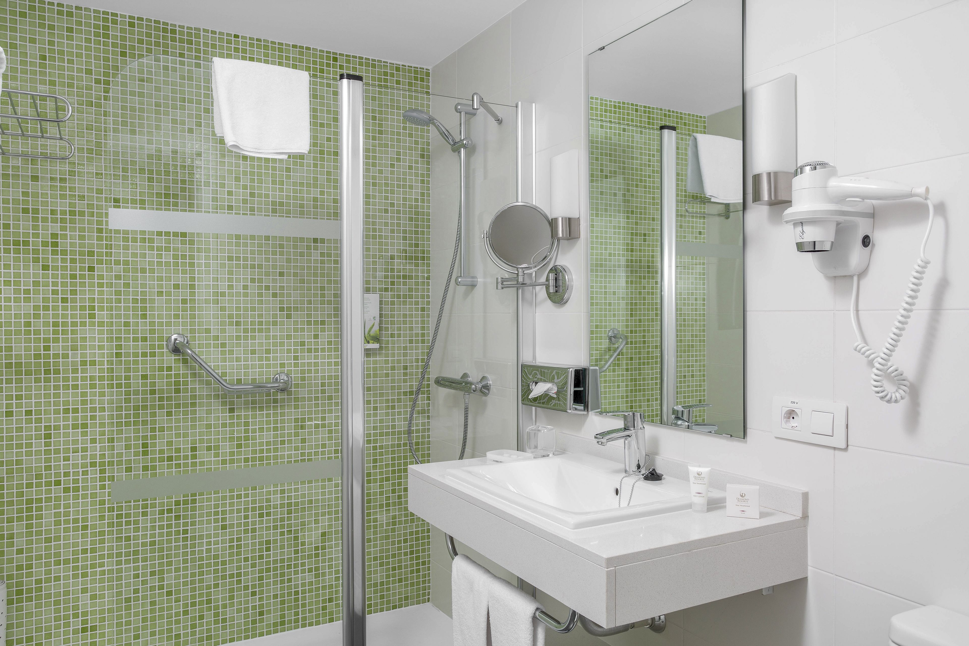 A bathroom with a glass shower enclosure, a white sink, a mirror, and a hairdryer mounted on the wall.