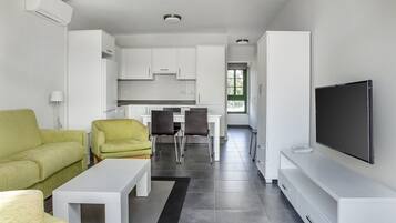 Una sala de estar moderna con sofá, sillas, una mesa de centro, televisor y una cocina al fondo.