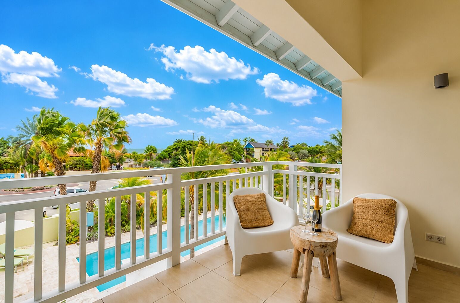 A balcony with a pool view, white chairs, and a small wooden table.