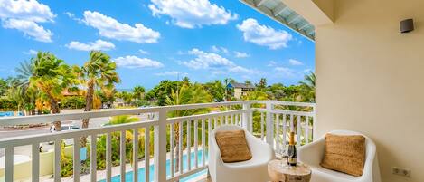 A balcony with a pool view, white chairs, and a small wooden table.