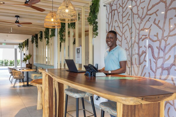 A reception area with a wooden counter, bar stools, a laptop, and a telephone. - Dolphin Suites & Wellness Curacao (Willemstad)