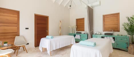A room with two beds, a wooden ceiling fan, a wooden wardrobe, a teal vanity, and a potted plant.