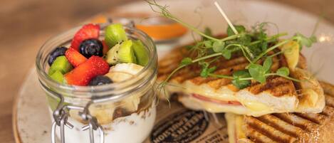 A plate with a sandwich, a glass jar of yogurt with fruit, and a small bowl of sauce.