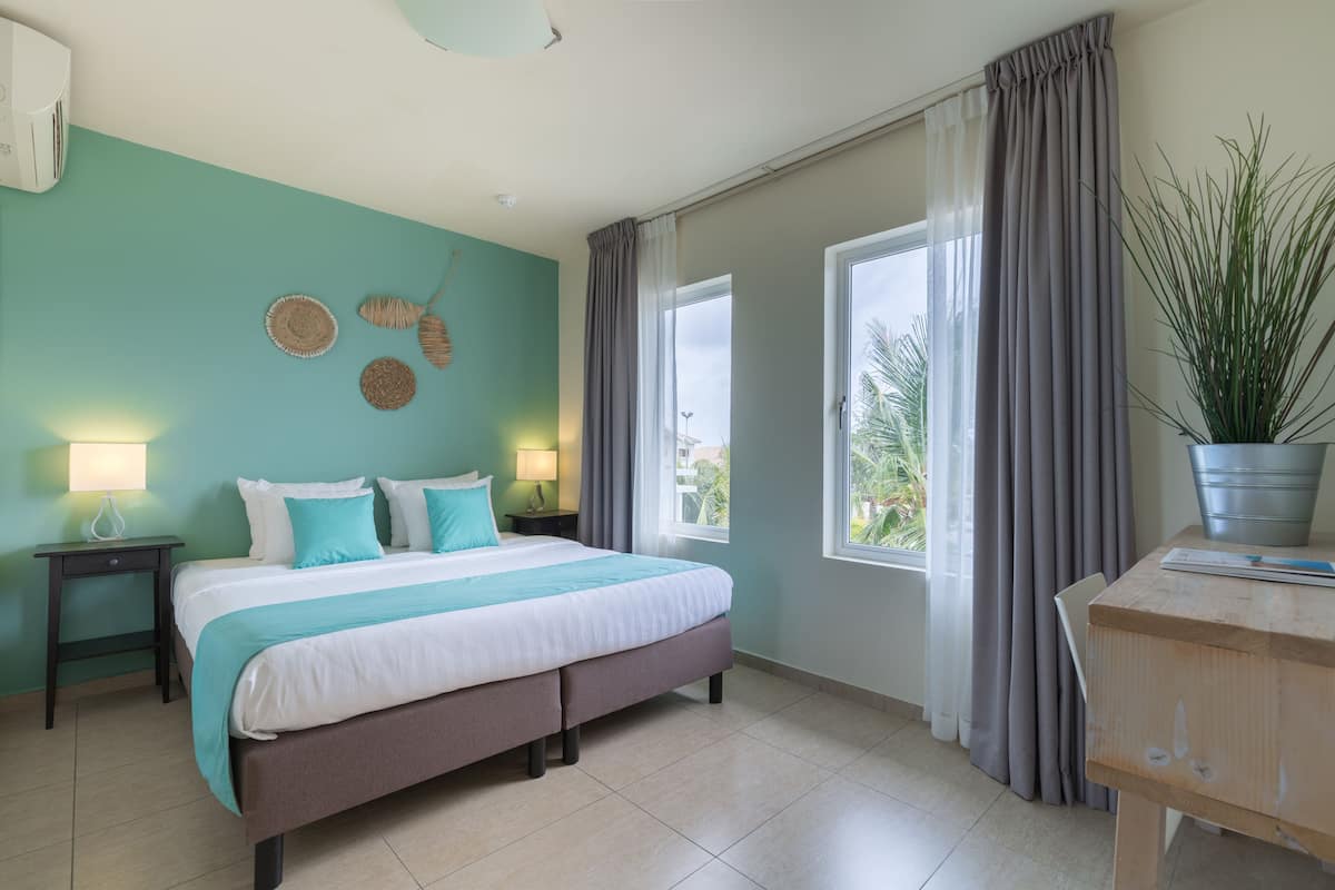 Un dormitorio con cama, mesitas de noche, una ventana con cortinas, una planta en maceta y vistas al exterior.