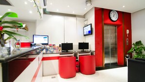 A modern hotel lobby with a reception desk, two computer monitors, a clock, and a red elevator. - Patong Terrace (Patong)