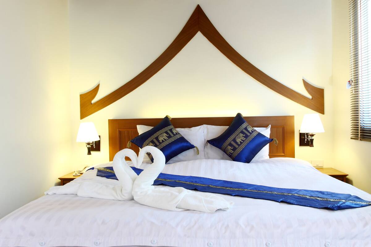 A hotel room with a large bed, two wall-mounted lamps, and a wooden headboard.