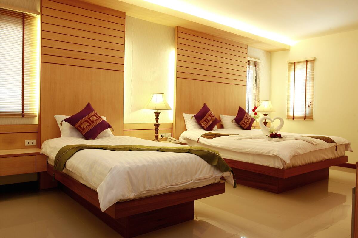 A hotel room with two wooden beds, each with white bedding and purple pillows. There are bedside tables with lamps and a wall-mounted phone.