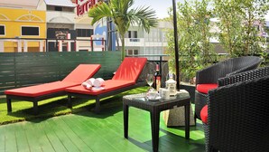 A patio area with two red lounge chairs, a wicker table with a bottle and glasses, and a red umbrella. - Patong Terrace (Patong)