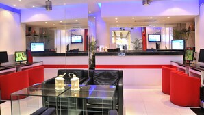 A modern reception area with glass tables, red and black seating, and multiple screens displaying content. - Patong Terrace (Patong)