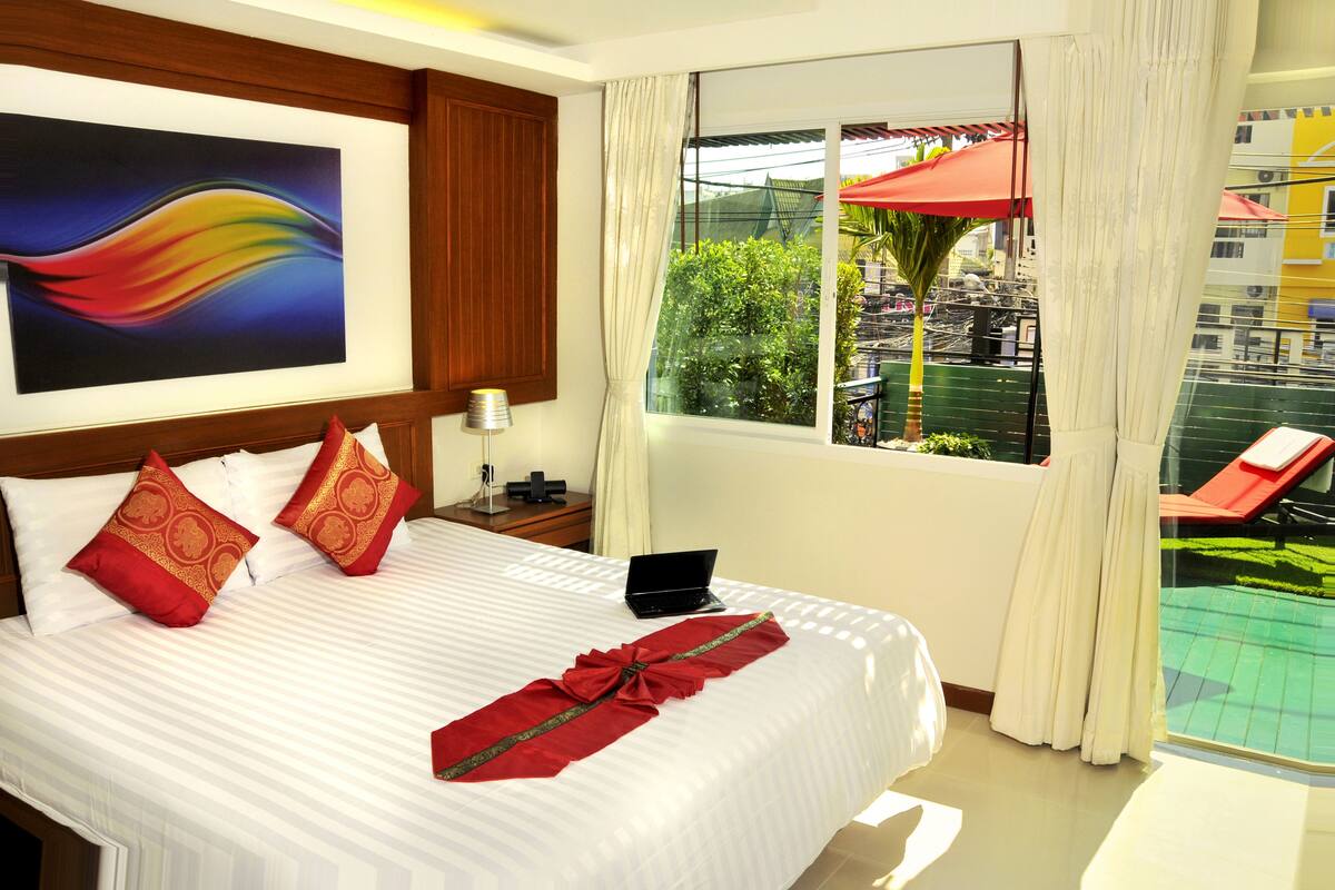 A hotel room with a bed, a laptop, a painting, and a view of a pool and outdoor area.
