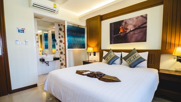 A hotel room with a large bed, a bathroom with a mirror and sink, and a painting on the wall. - Patong Terrace (Patong)