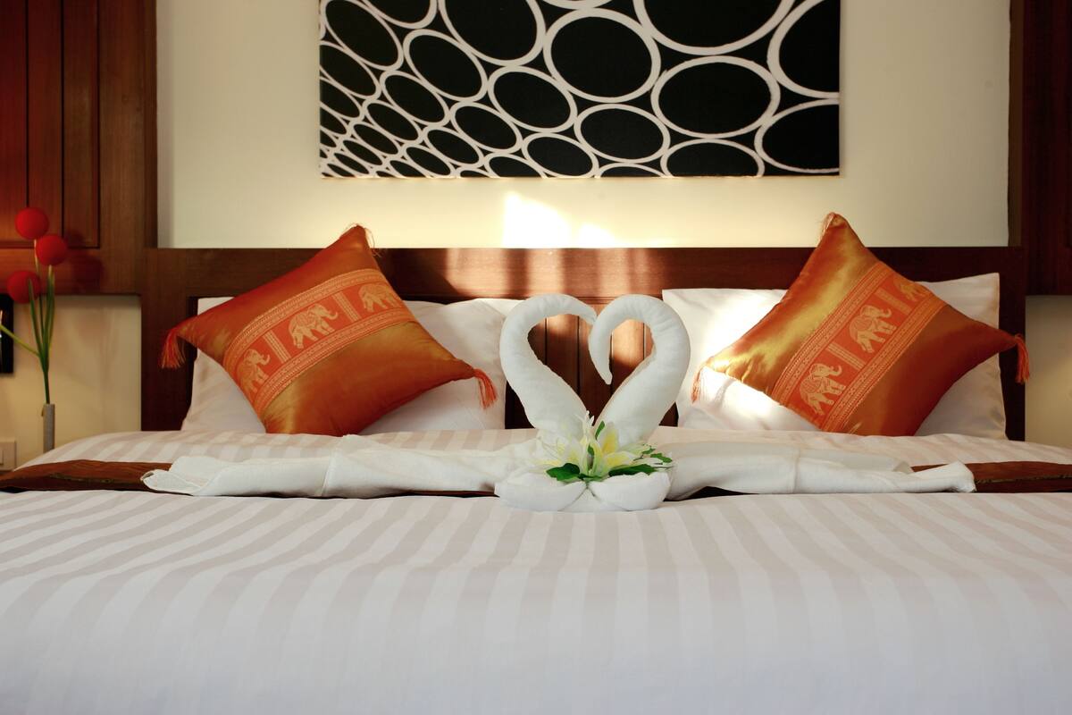 A hotel room with a bed featuring a heart-shaped towel arrangement and two pillows with a lion design.