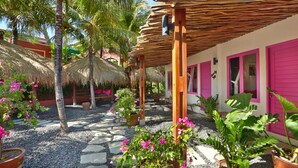 Un jardín tropical con techos de paja, palmeras y puertas rosadas vibrantes.