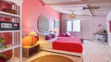 A bedroom with a bed, bedside tables, a lamp, a shelf with a basket, a wall clock, and a door.
