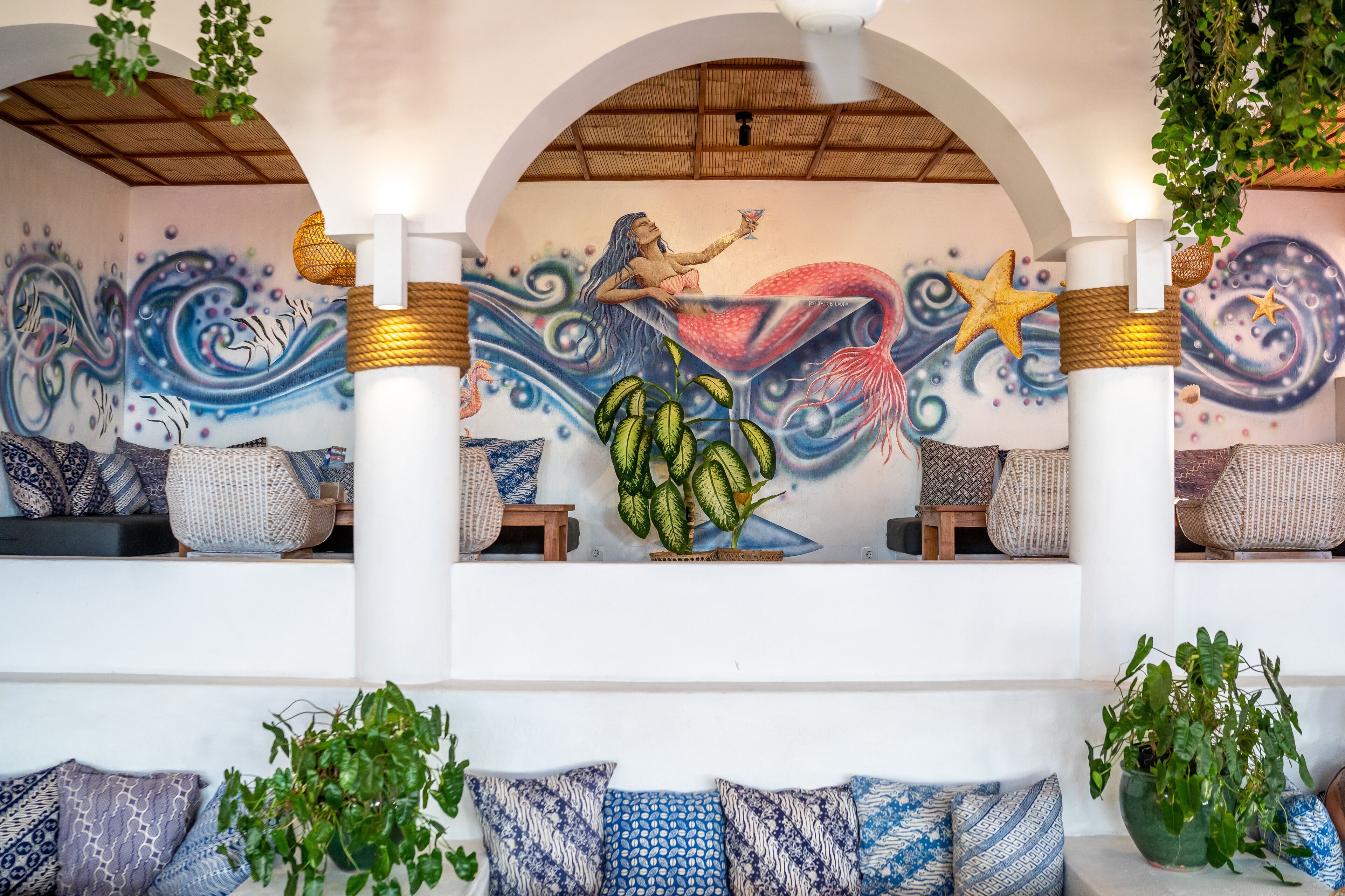 A mural of a mermaid with a starfish, a ceiling fan, and a seating area with patterned cushions.