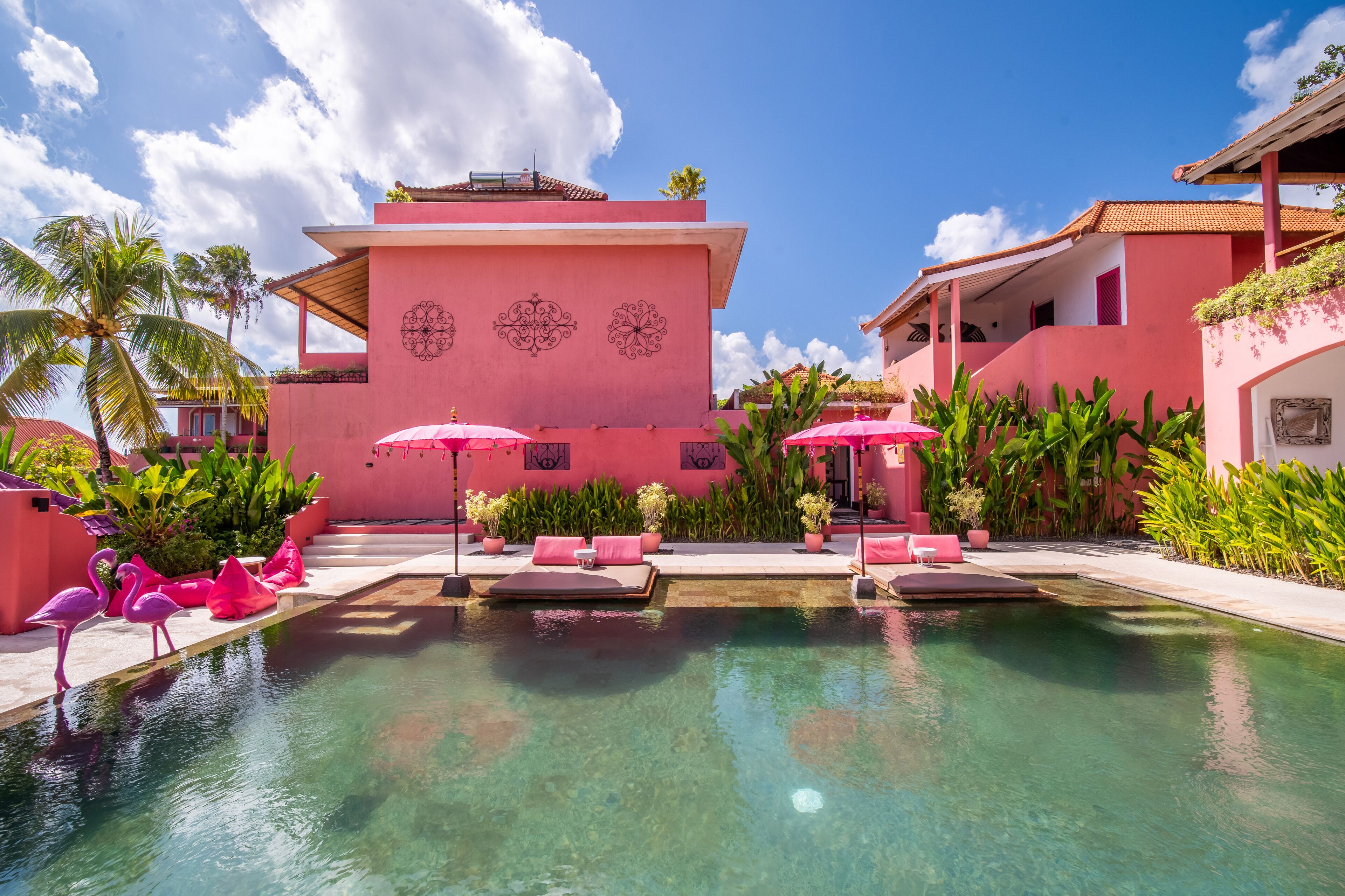 A pool area with pink flamingo statues, lounge chairs, and umbrellas.