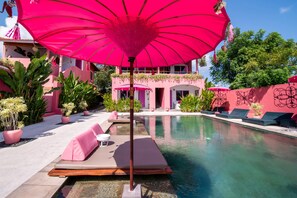 A poolside area with pink umbrellas, lounge chairs, and potted plants.