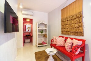 A room with a red bench, a white shelf, a wall-mounted TV, and a red door leading to a bathroom.