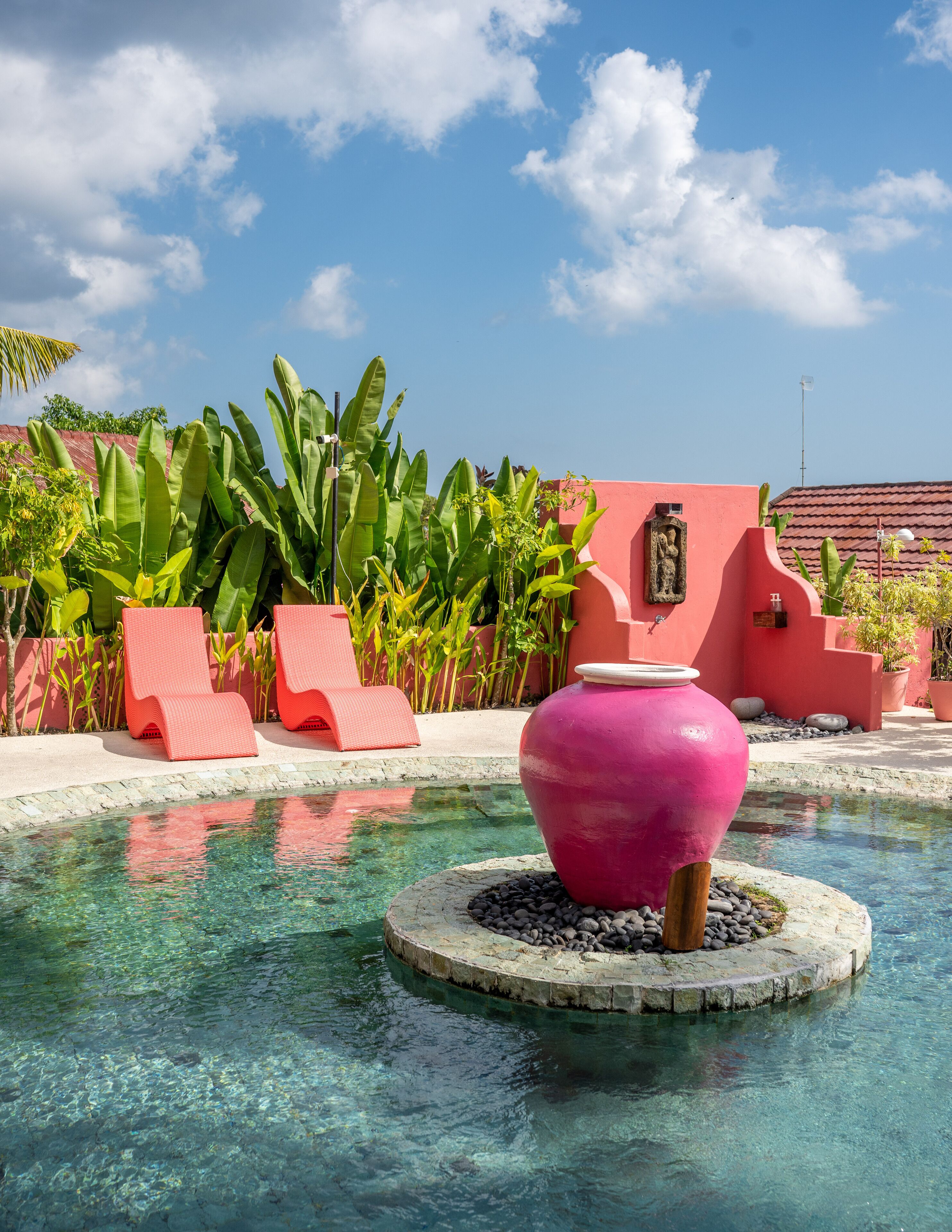 A pool with clear water, surrounded by red lounge chairs and tropical plants.