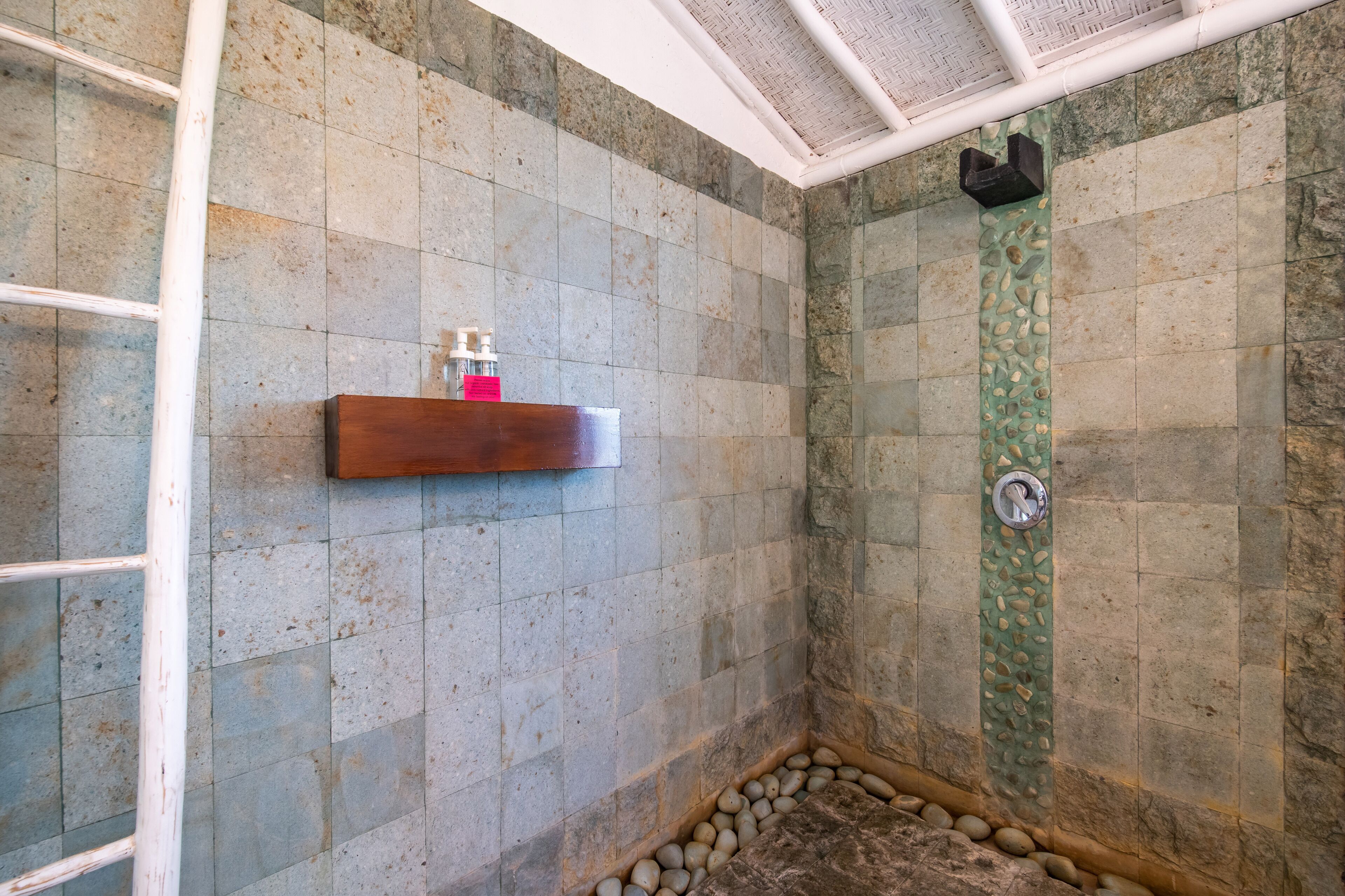 Un espace douche avec des carreaux de pierre, une étagère en bois pour les articles de toilette et un mur décoratif vert.