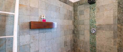 Un espace douche avec des carreaux de pierre, une étagère en bois pour les articles de toilette et un mur décoratif vert.