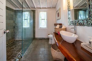 Un baño con cabina de ducha de vidrio, un lavabo blanco, un mueble de tocador de madera y un espejo decorativo.