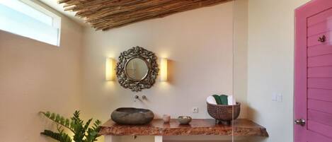A bathroom with a wooden ceiling, a mirror with ornate frame, a sink with decorative bowls, and a pink door.
