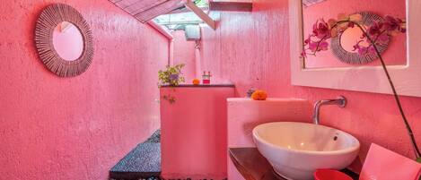 Ein Badezimmer mit rosa Wand, Waschbecken in Weiß, einem Spiegel und einer roten Tasse.