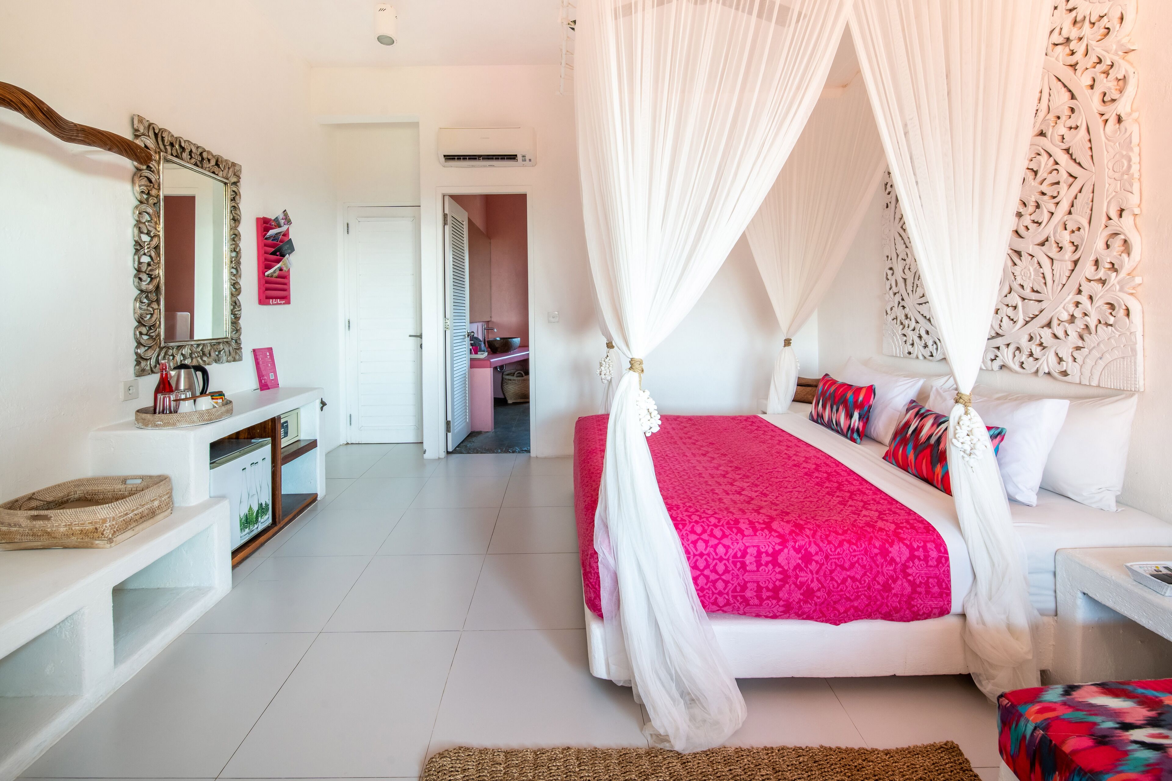 A bedroom with a four-poster bed, a vanity with a mirror, and a kitchenette in the background.