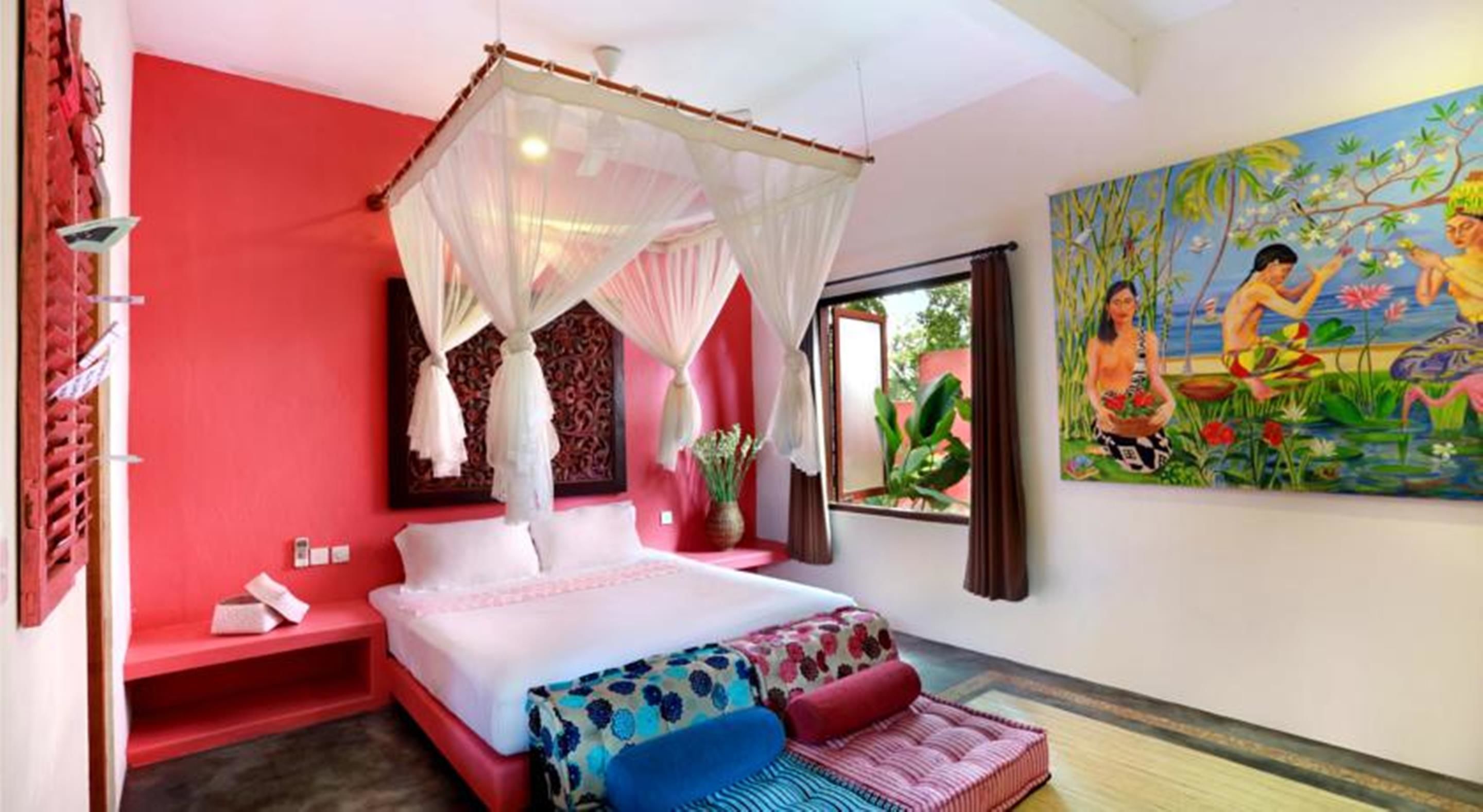 Un dormitorio con una cama, una pared roja, un cuadro y una ventana.