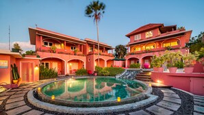 Un hotel de varios pisos con piscina central, rodeado por un sendero de piedra y exuberante vegetación.