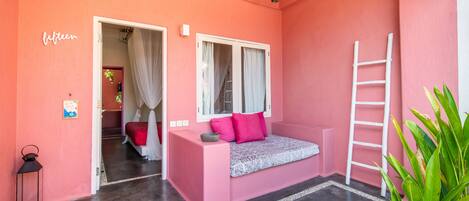 A pink room with a bed, a ladder, a ceiling fan, and a door leading to another room.