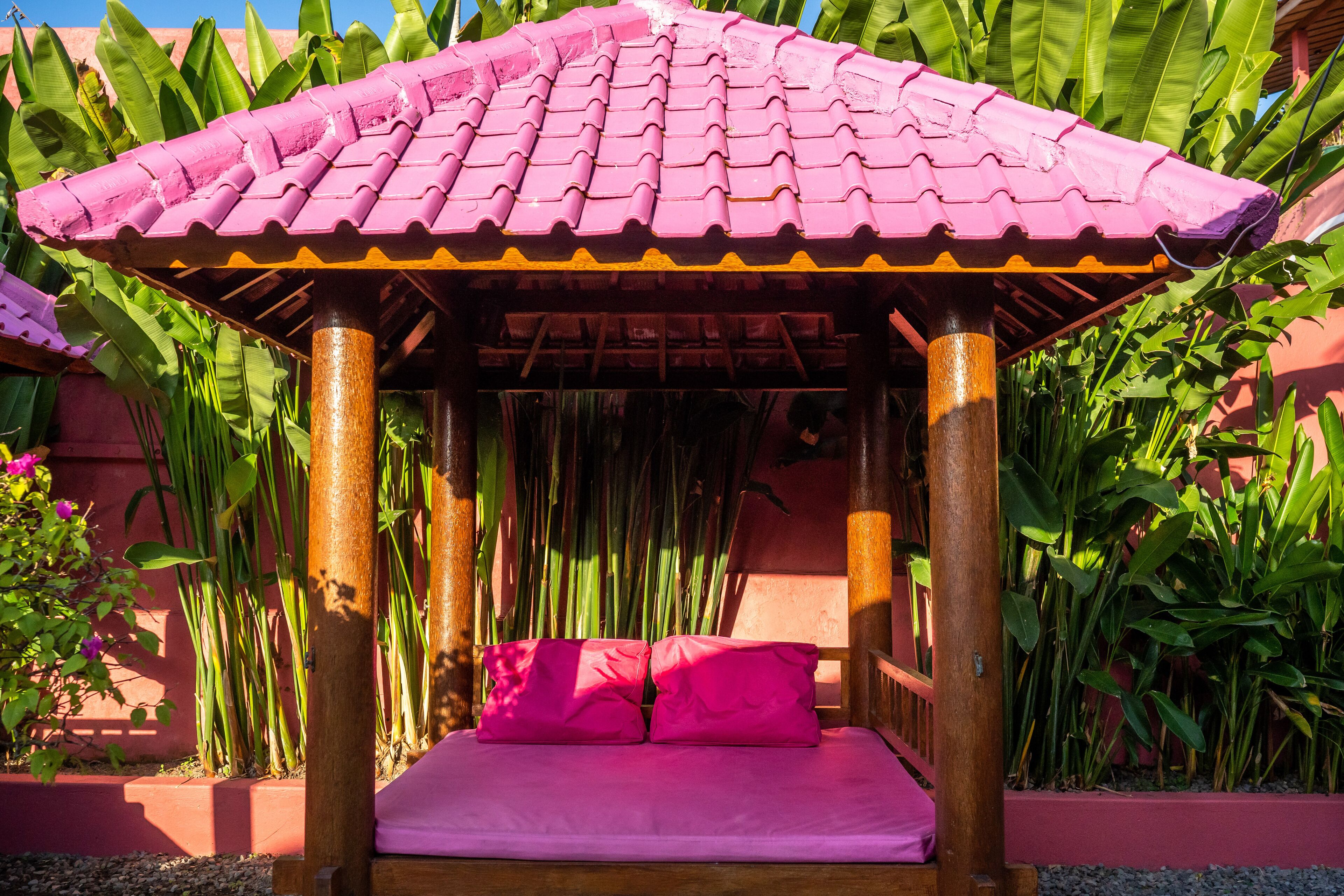 Un kiosque en bois avec un toit rose et un lit avec une literie rose.