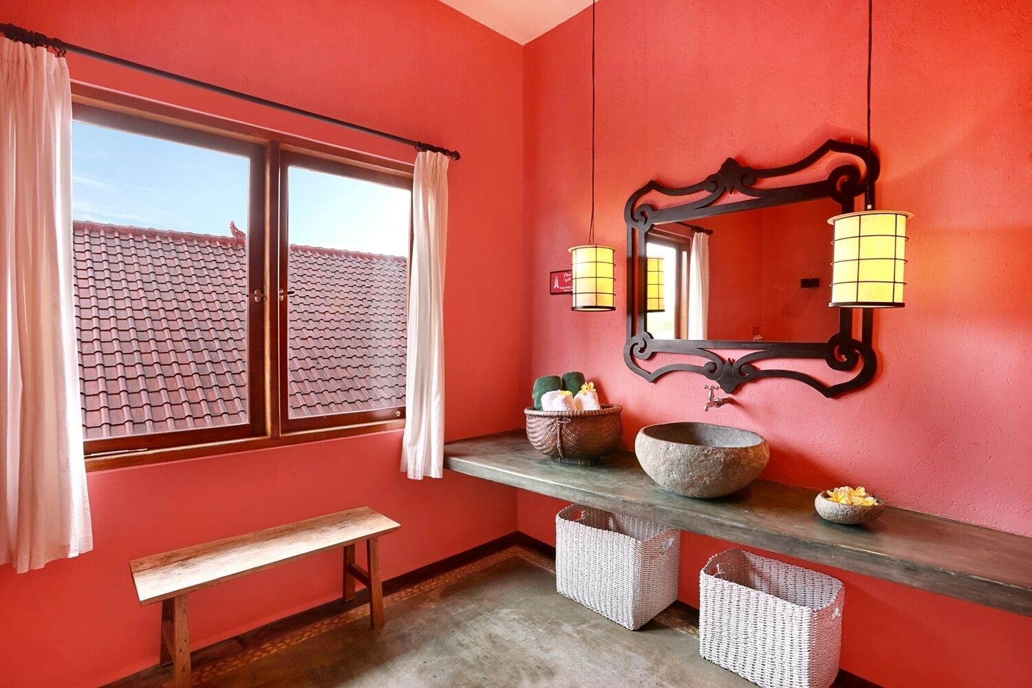Ein Badezimmer mit roter Wand, einer Holzbank, einem großen Spiegel und zwei Wandleuchten.